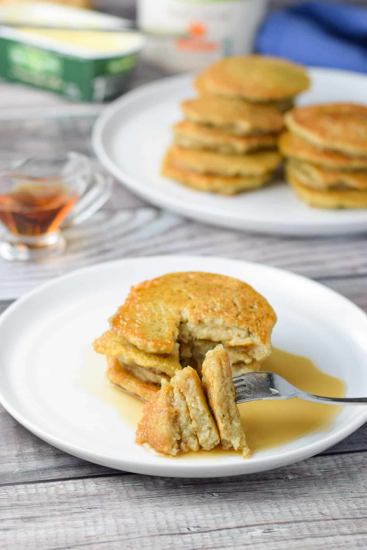 a fork with cut pancake triangles resting in syrup with a plate of pancakes in back