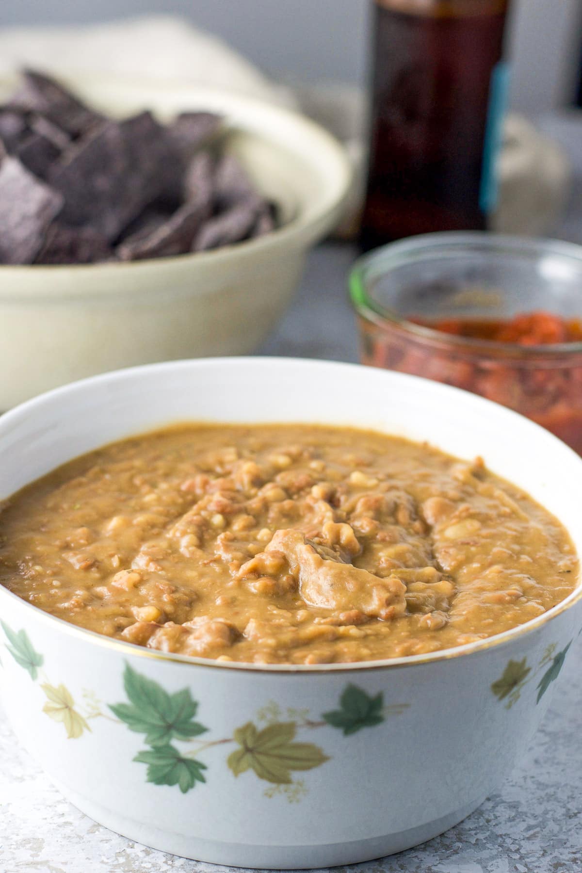 a white bowl filled with beans with salsa, chips, and beer in back