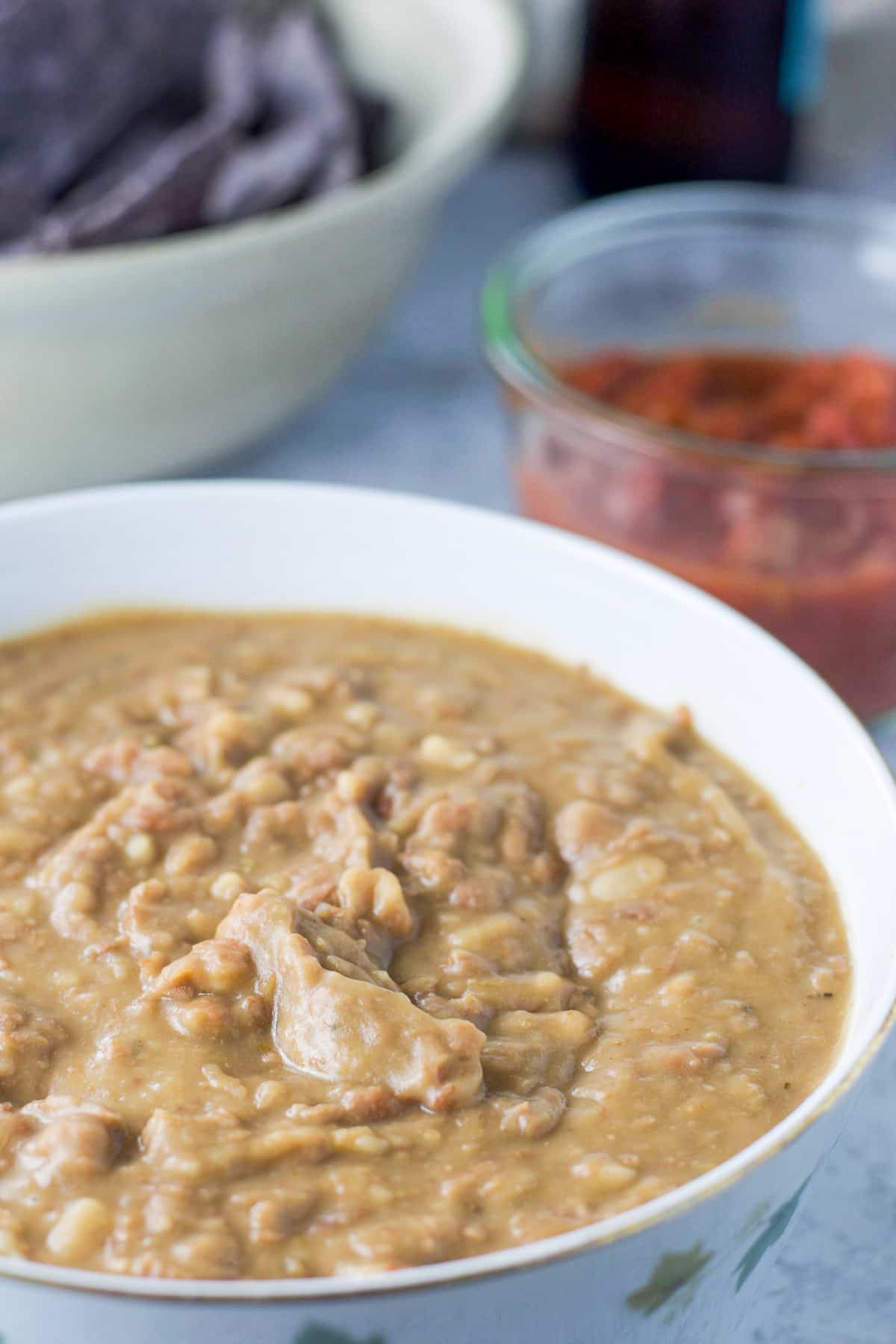 Close view of a bowl of beans with salsa, and chips in back