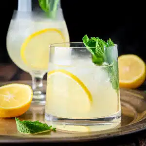 square photo of a metal platter with the two drinks on it with lemon and mint