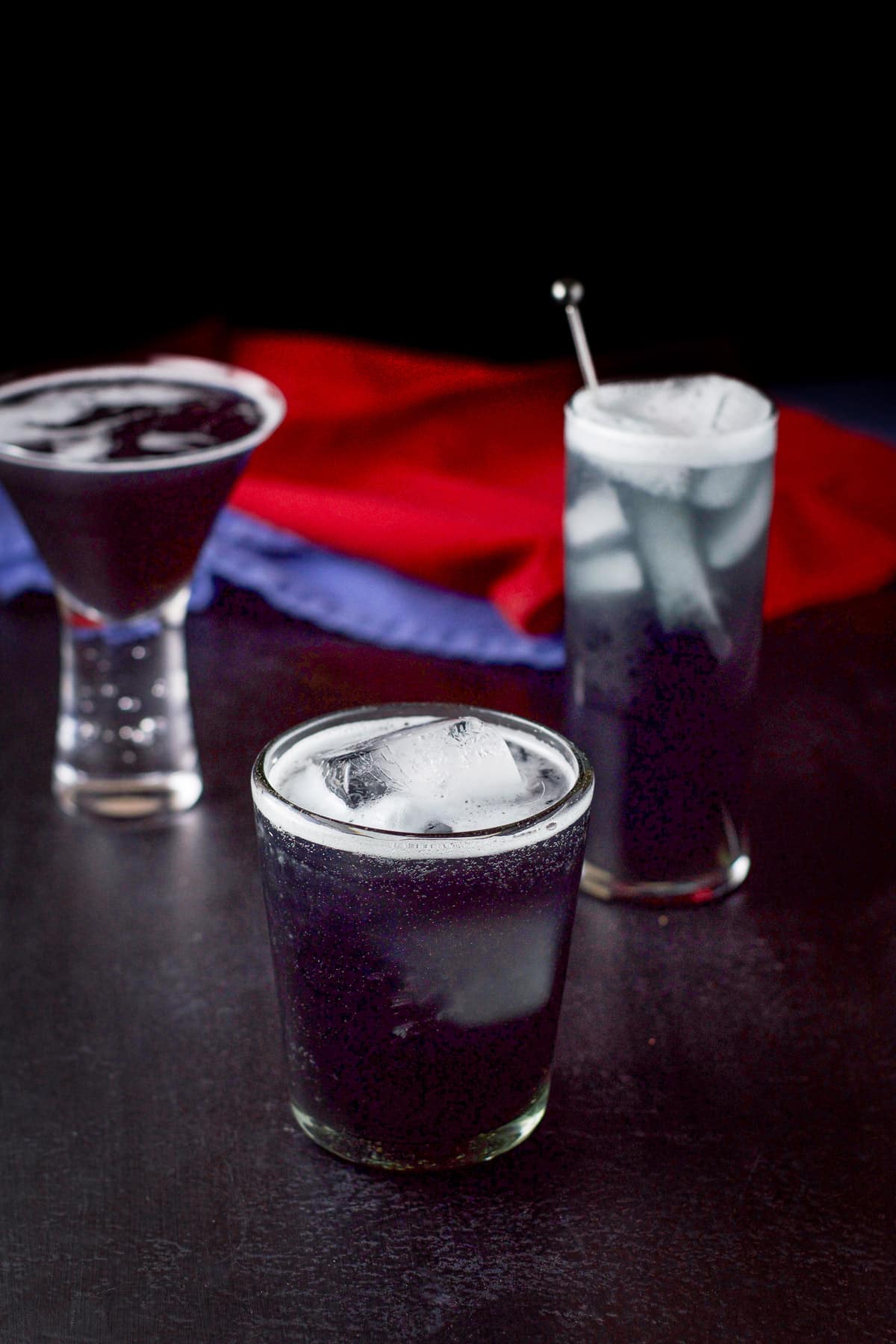 The double old fashioned glass in front of the other two filled with the purple rain cocktail