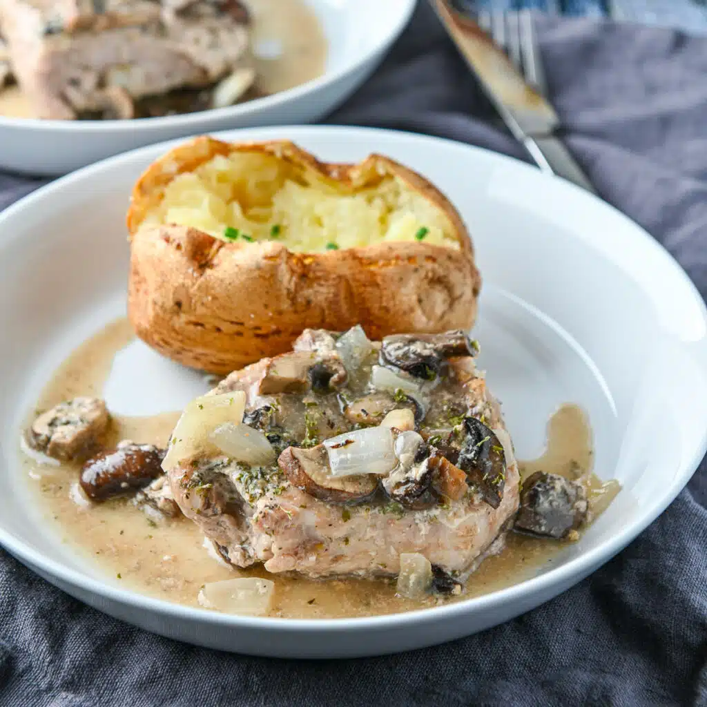 square photo of a white deep plate with a pork chop and mushrooms as well as a baked potato