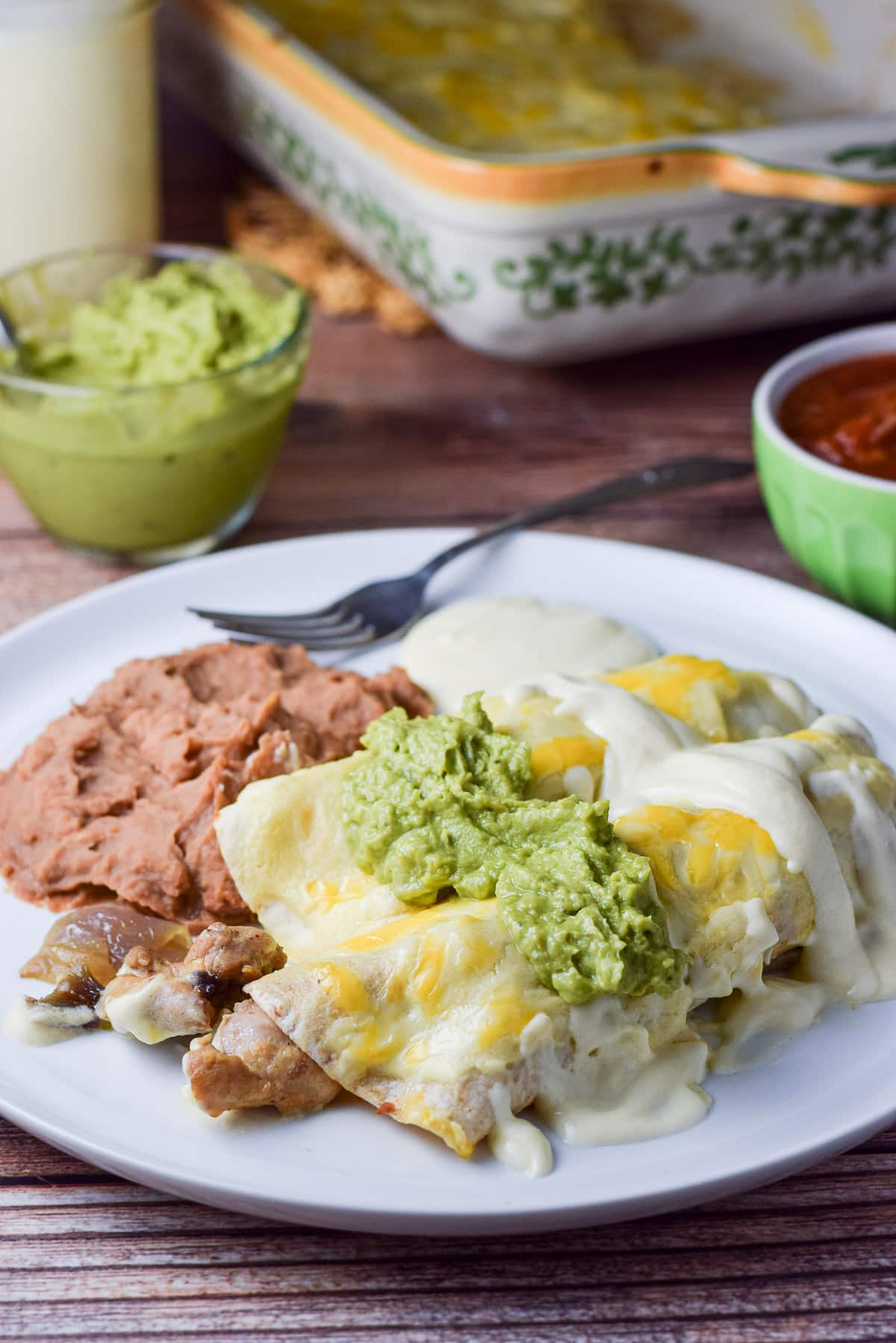 Close up of enchiladas on the white plate with beans, guacamole and salsa