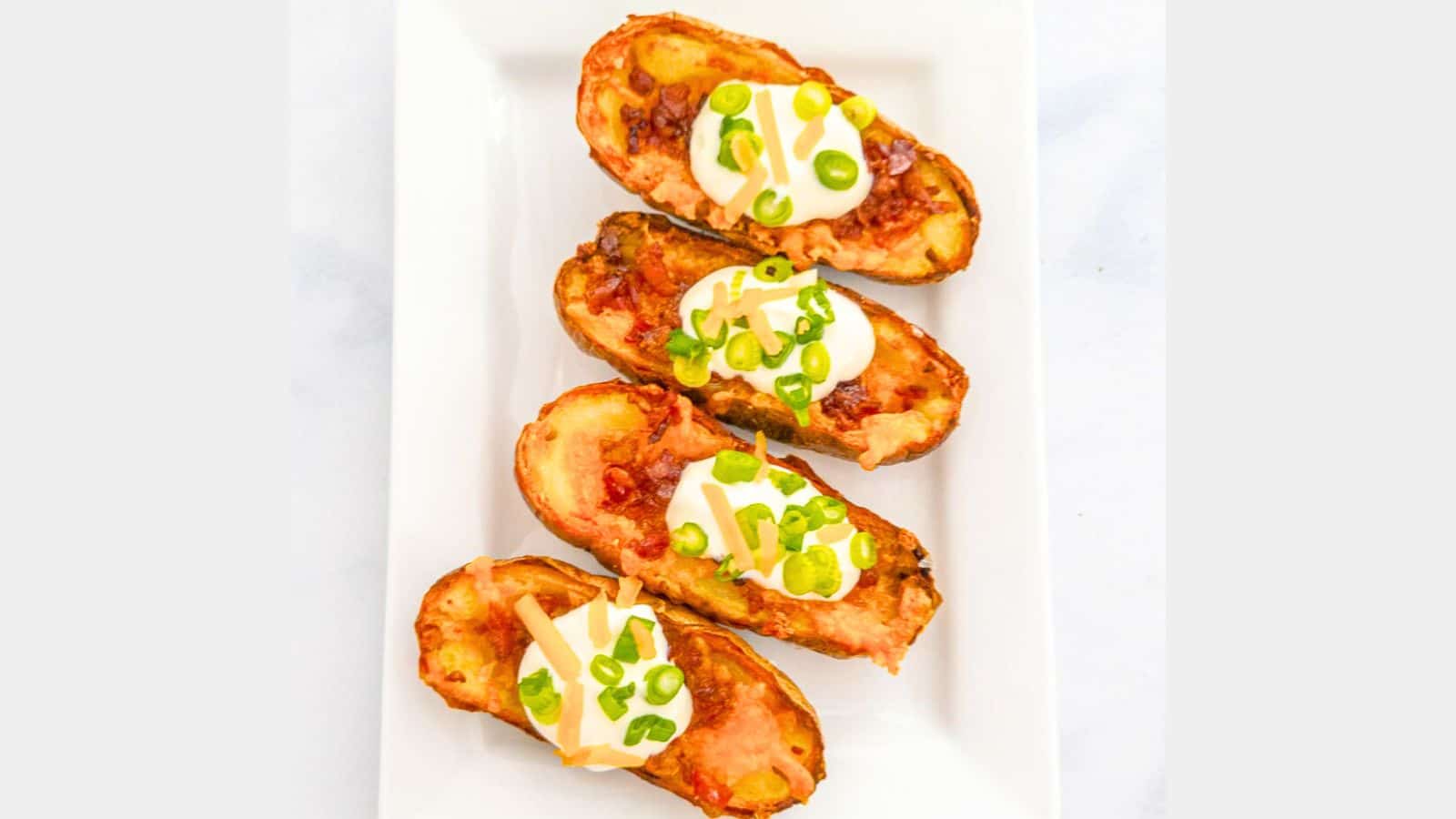 A rectangle plate with four potato halves on it with sour cream, cheese and chives