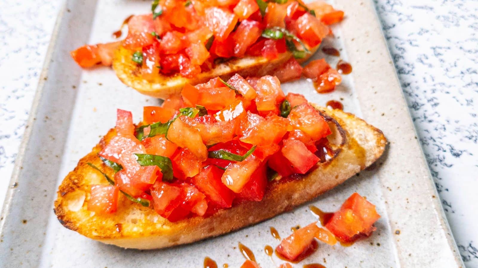 A rectangle platter with grilled bread and tomatoes on it