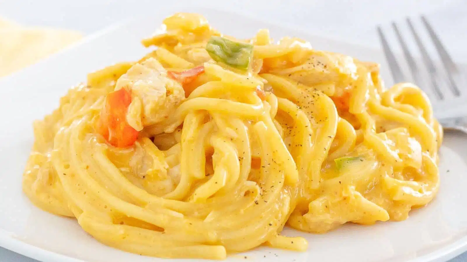 a white plate with a creamy spaghetti with vegetables and chicken