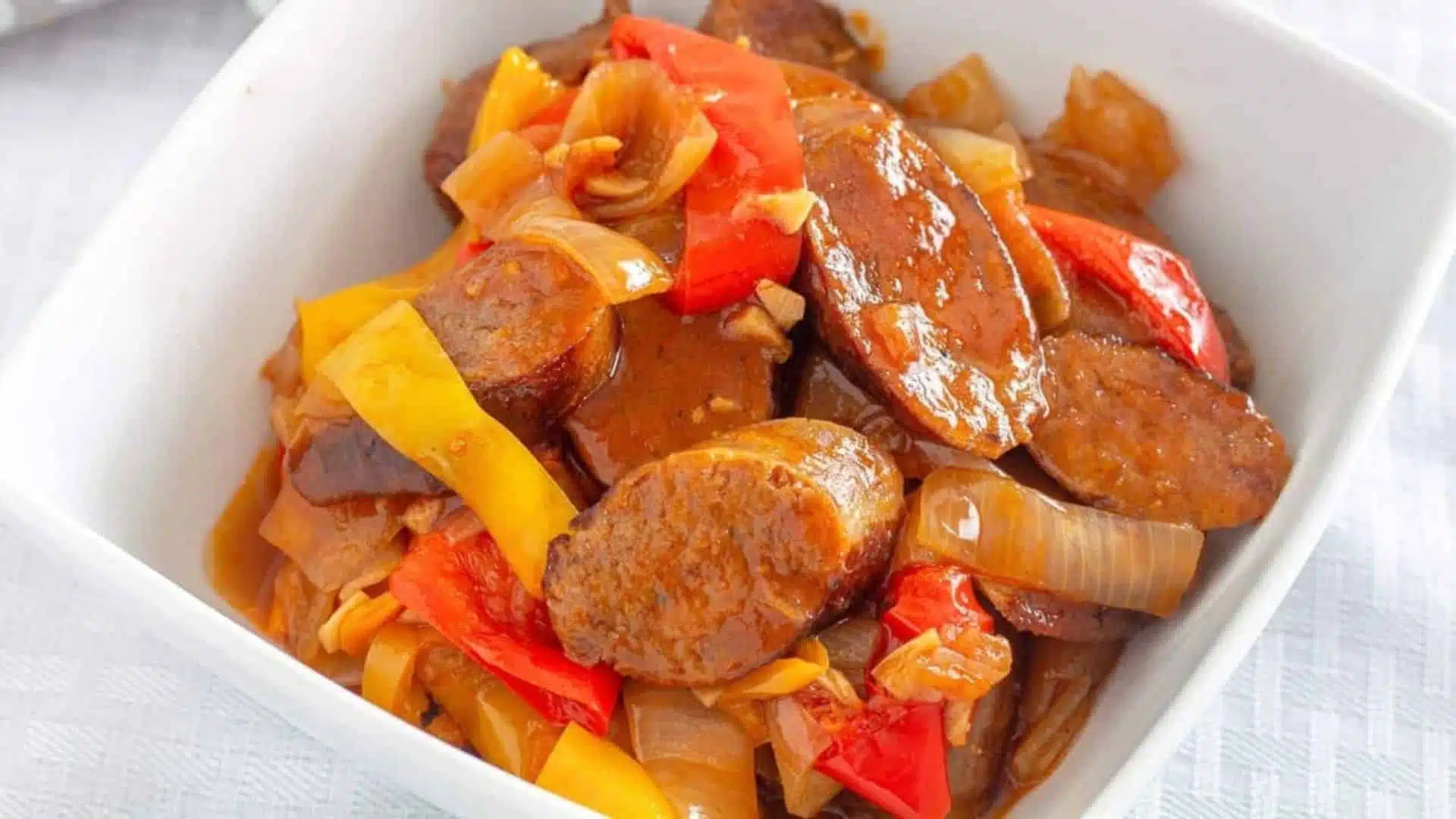 A white square deep plate with sausages, peppers and onions