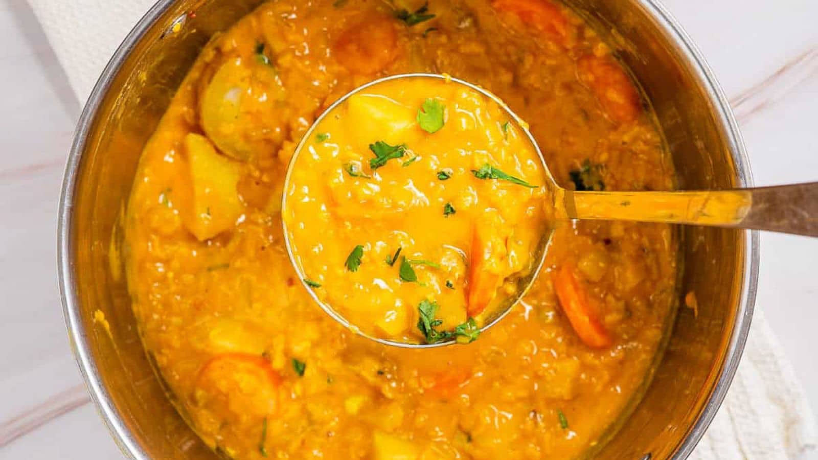 A ladle with the vegan orange soup in it over the pan of soup