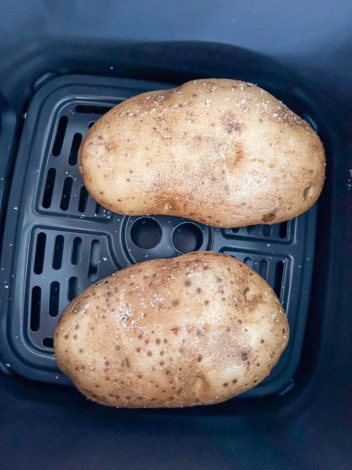 overhead view of two potatoes with oil and salt on it in an air fryer basket