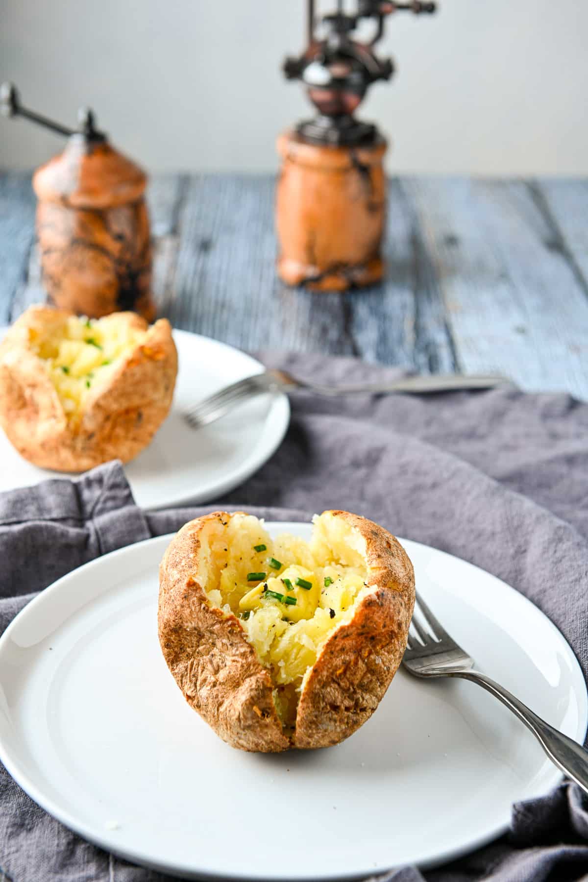 two white plates with cooked potatoes on them along with forks and a salt and peppers shaker
