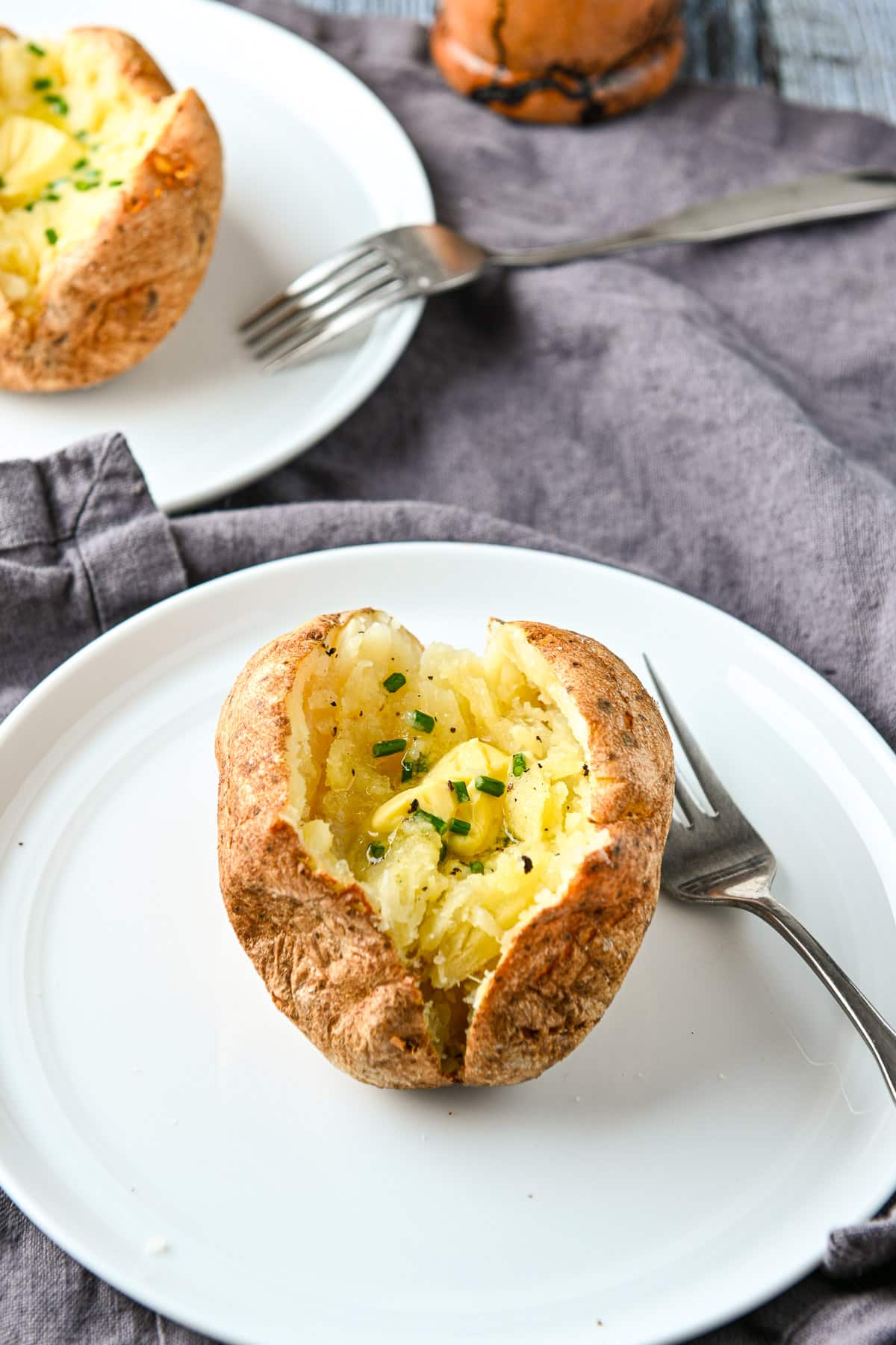 Two white plates with baked potatoes with chives and butter with forks on the plate