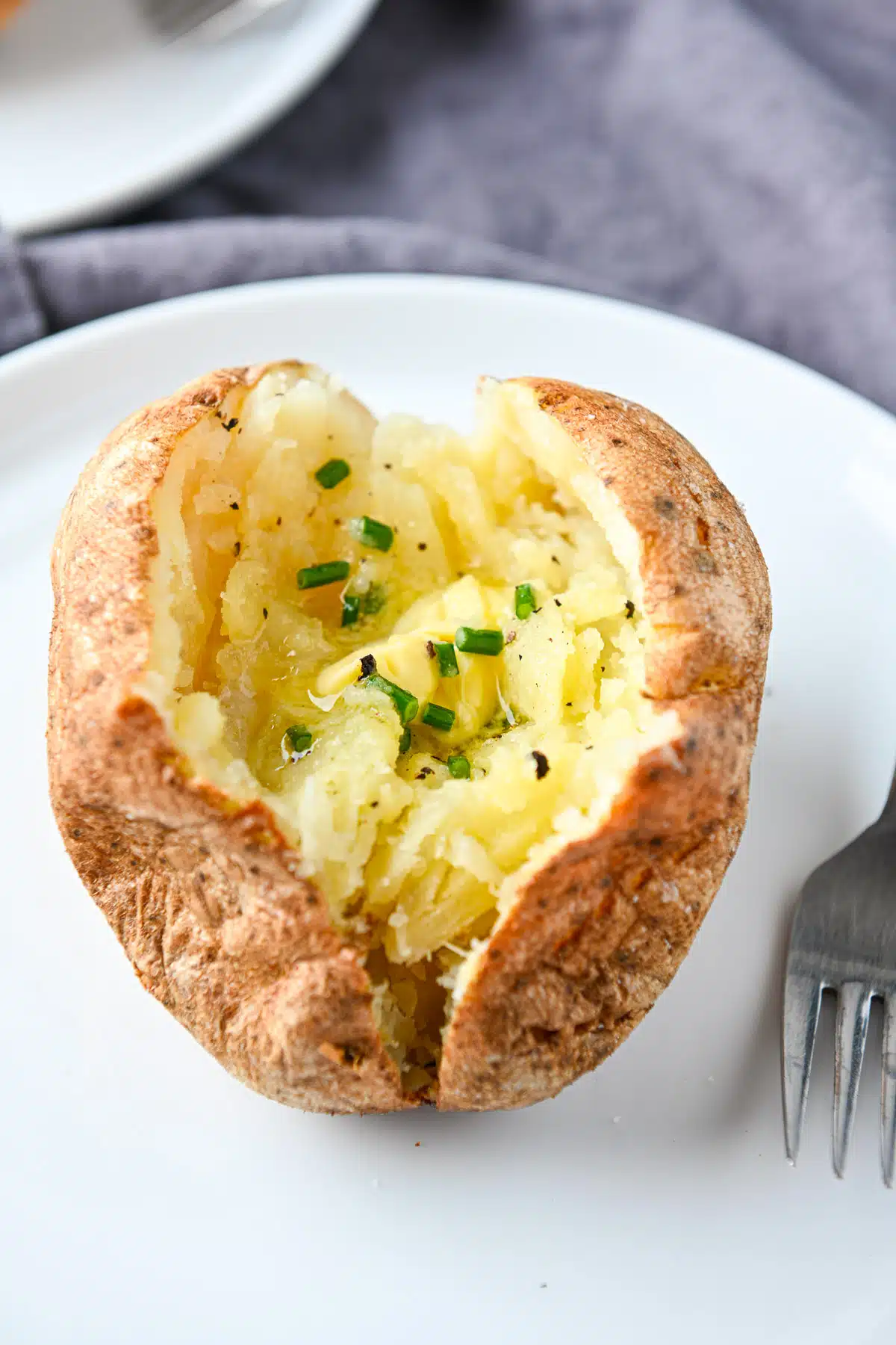 Close up of a split potato that has been baked and butter and chives on it