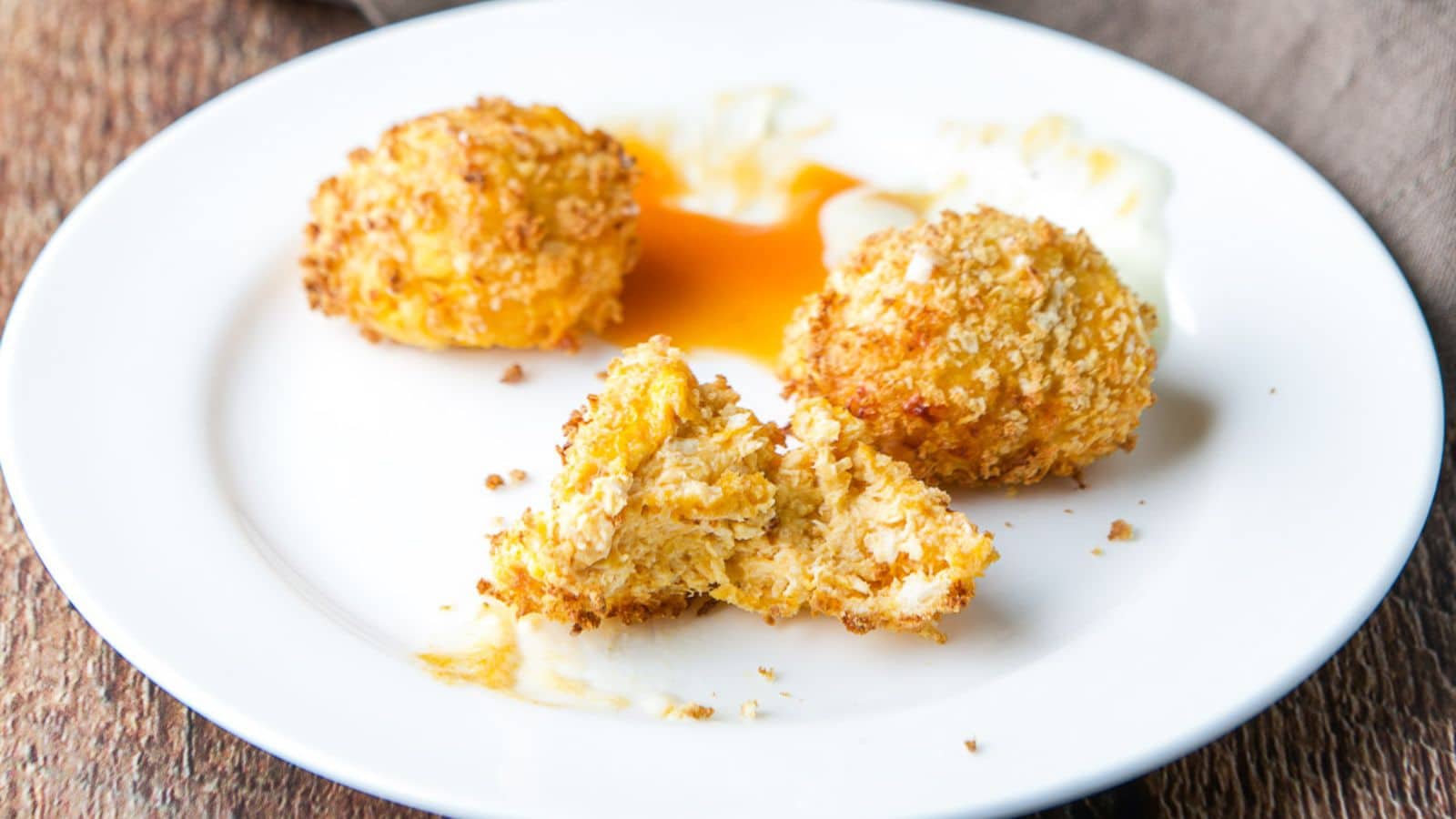 a white plate with three chicken bites on it. One with a bite taken out of it and sauce off to the side