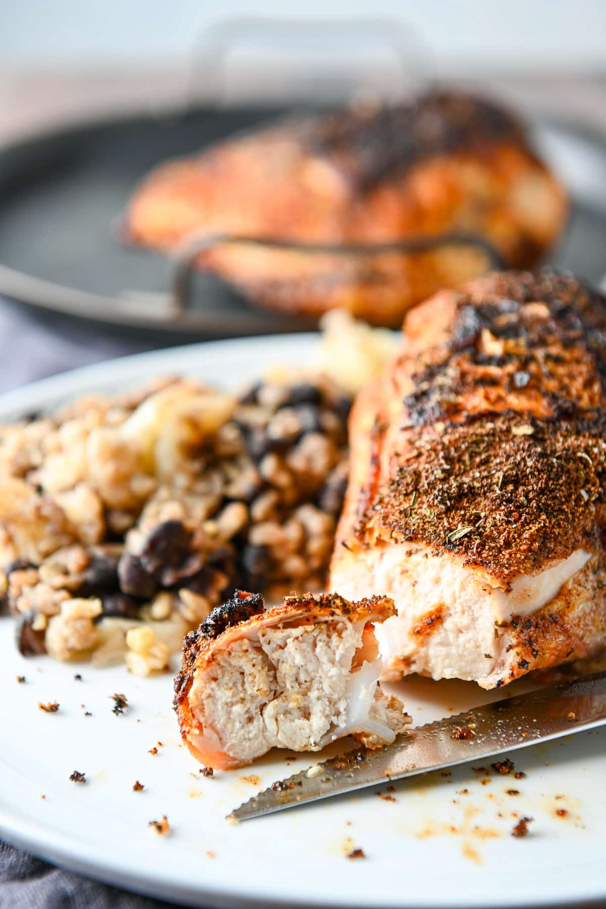 Close up of the chicken piece on a plate with the rest of the meal on it along with a chicken breast in the back