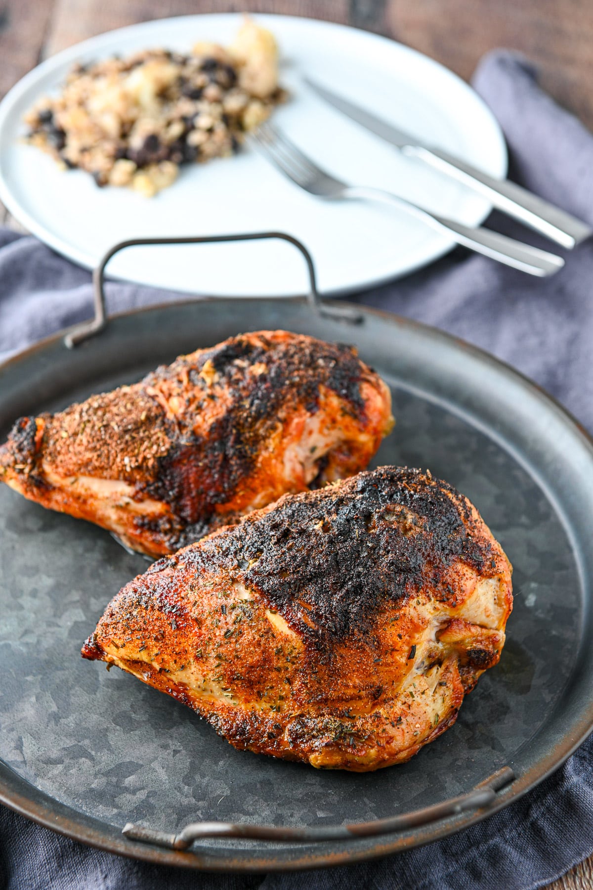 A metal round tray with the chicken breasts cooked in front of a plate with rice and beans on it