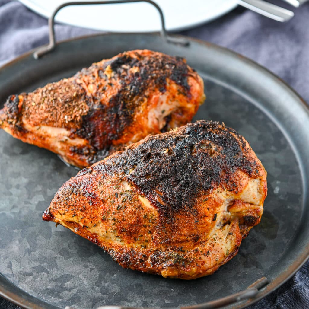 A metal round platter with two cooked, crispy skinned chicken breasts on it