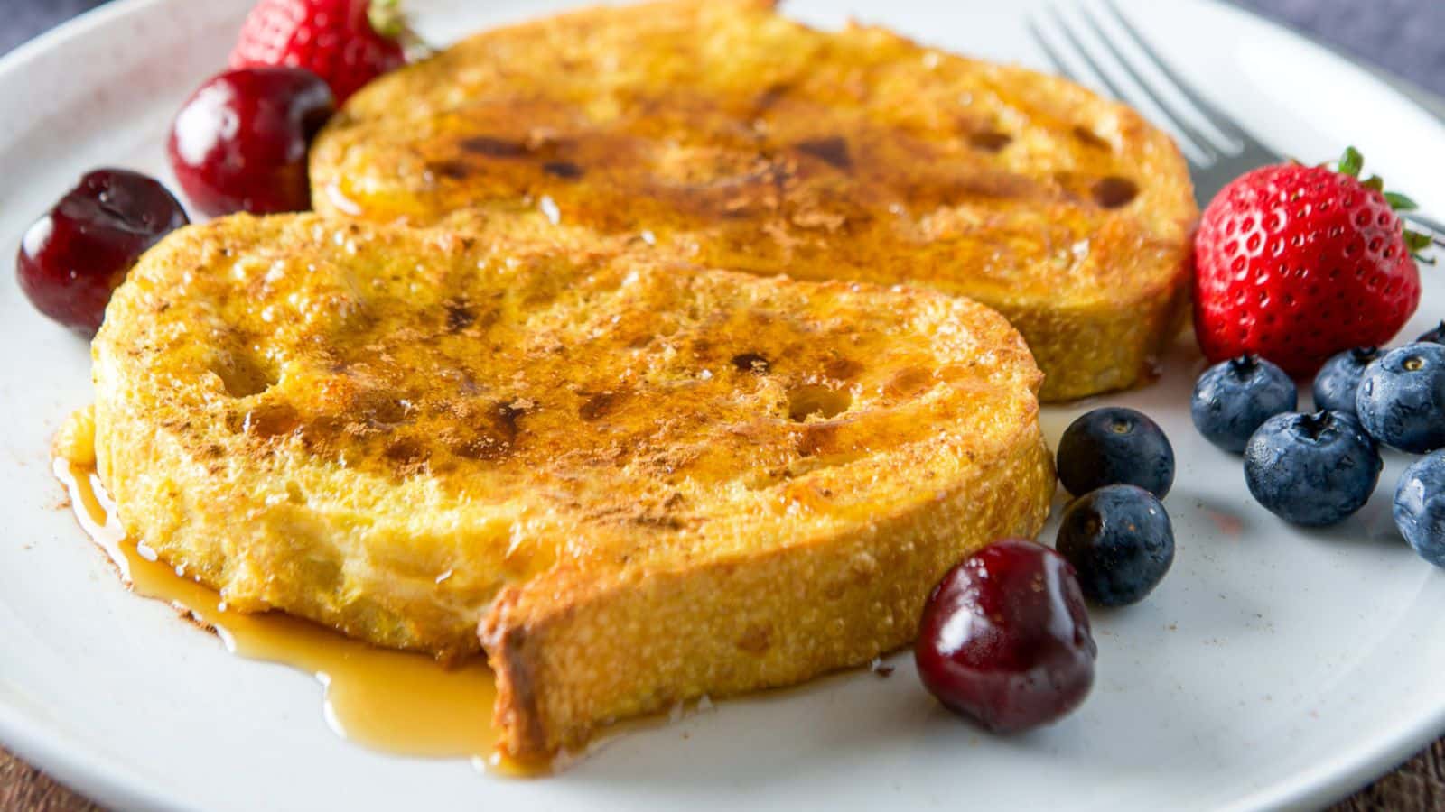 Fruit on a plate with two slices of french toast and maple syrup over them