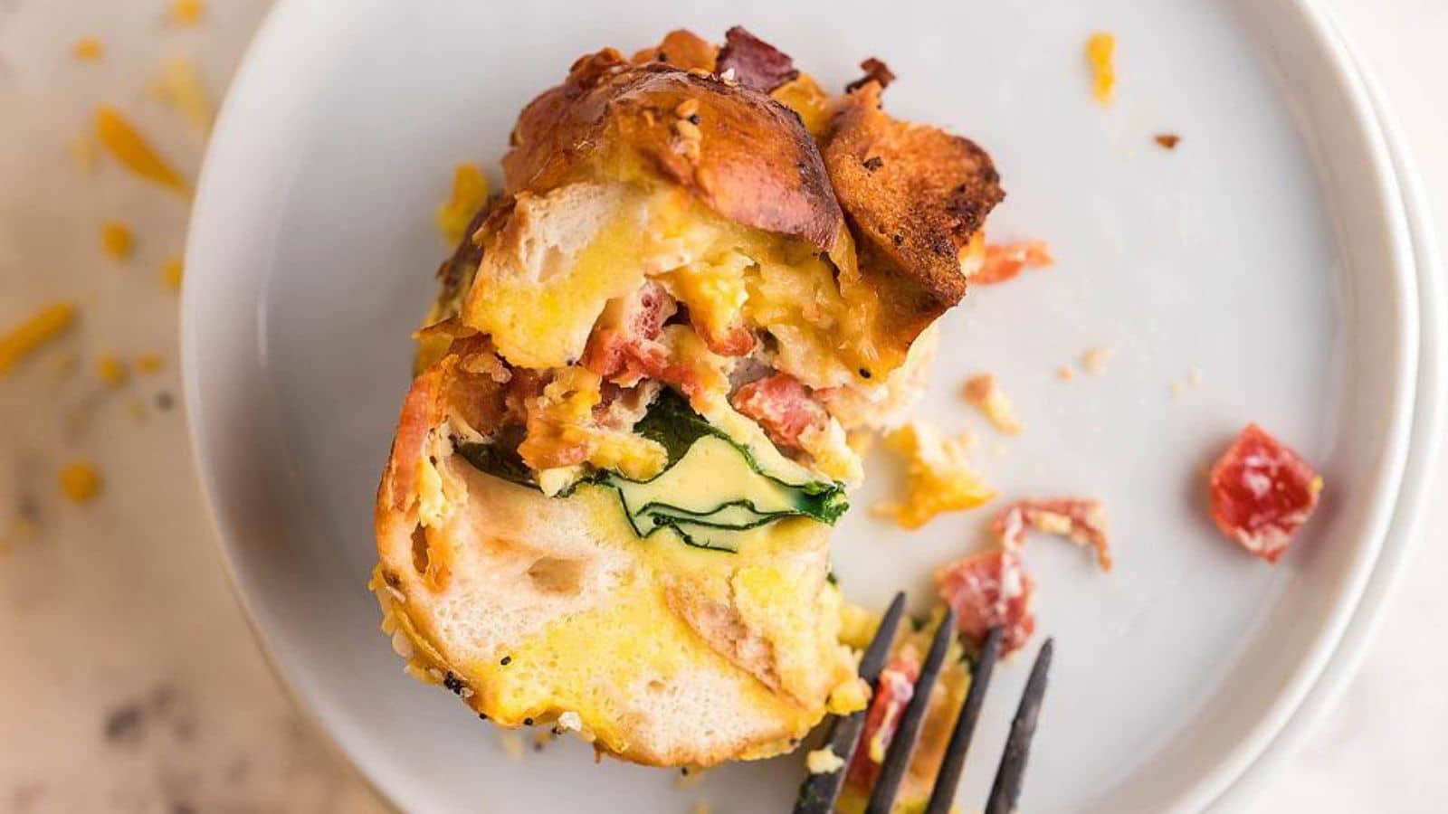 A white plate with a bagel filled with meat, egg and cheese