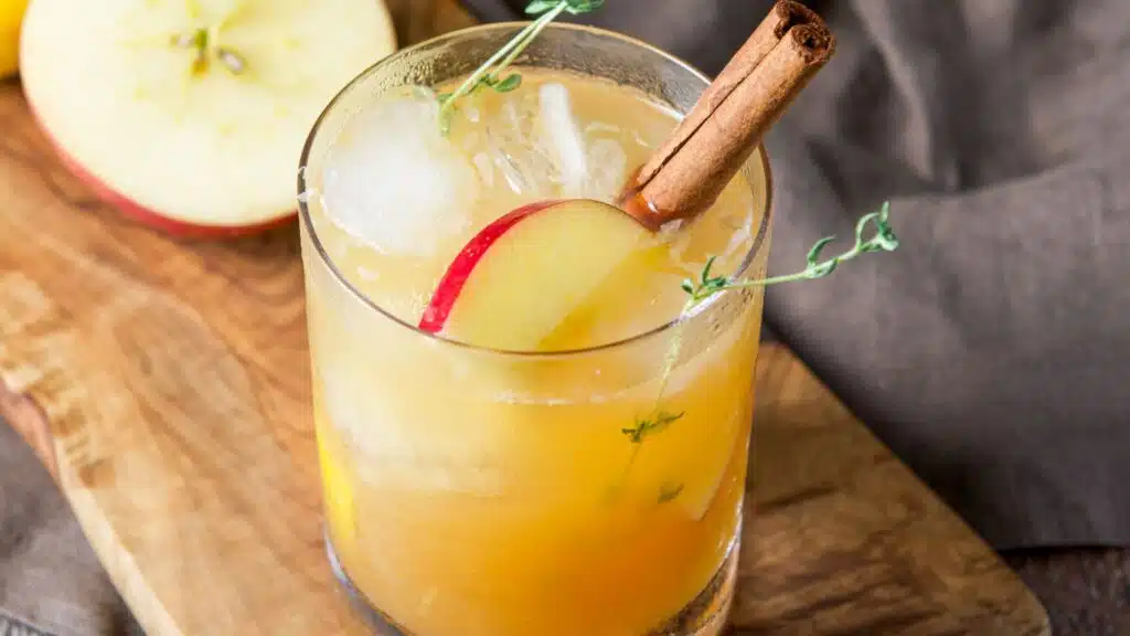 A cinnamon stick, apple slice and herbs in an apple cocktail on a board