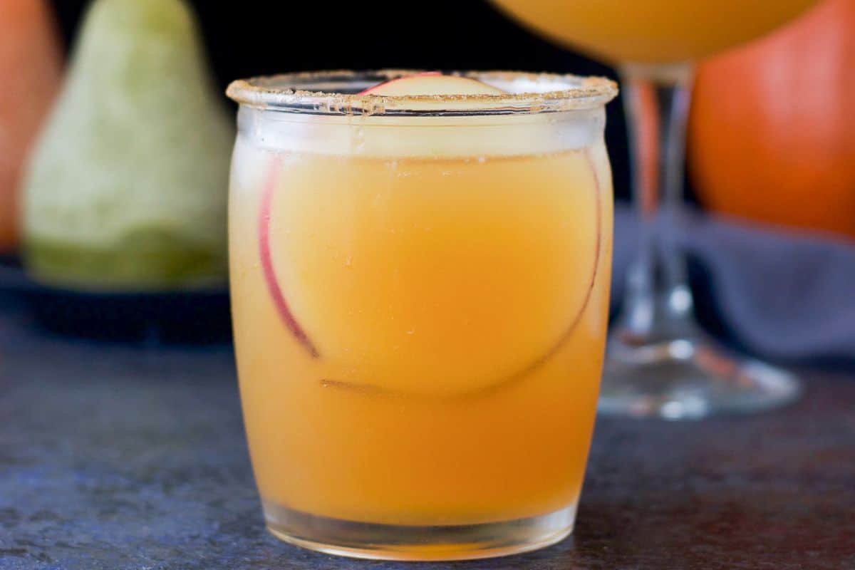 cinnamon sugar on the rim of a glass filled with the apple cider drink with an apple wheel in the cocktail
