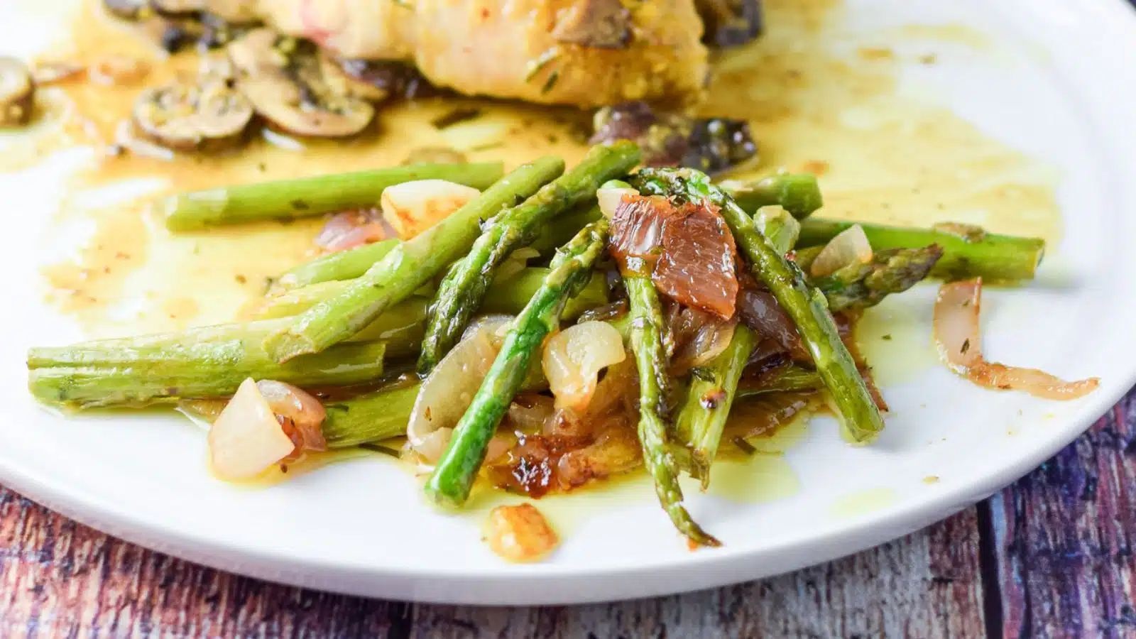 A plate with asparagus and onions on it with chicken in the back