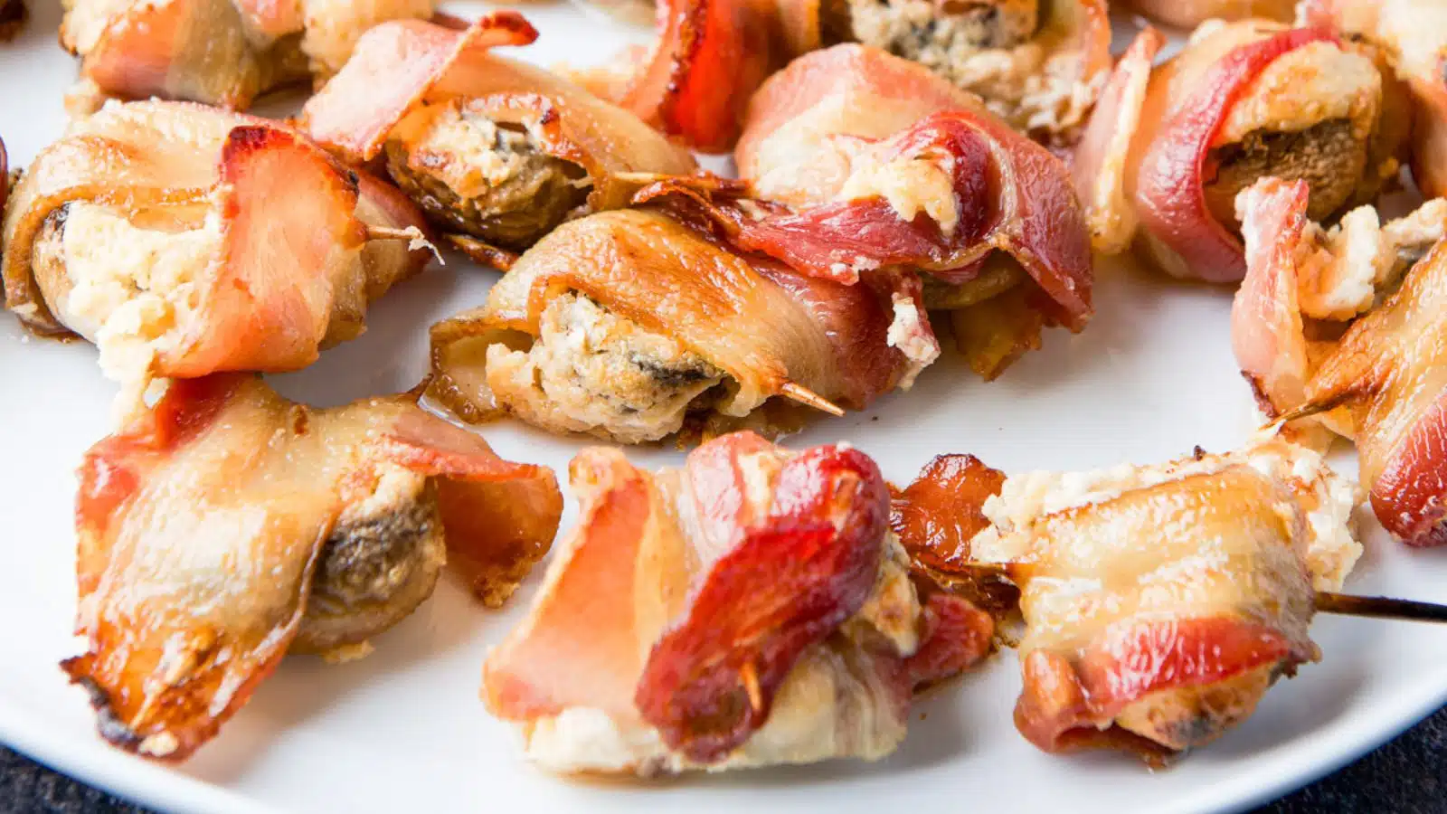 A white plate with bacon wrapped around a stuffed mushrooms