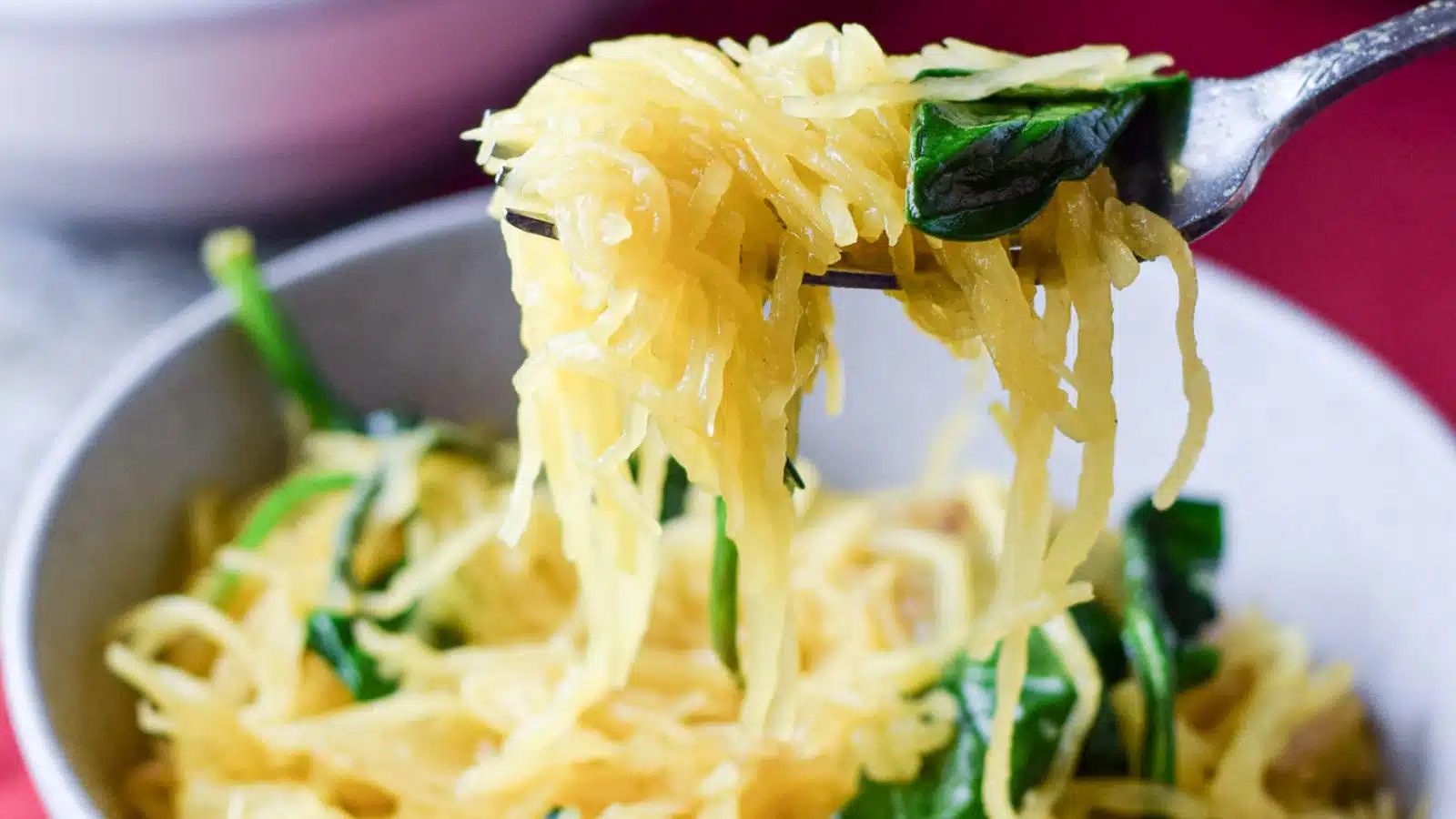A fork with spaghetti squash ad spinach on it held over the bowl