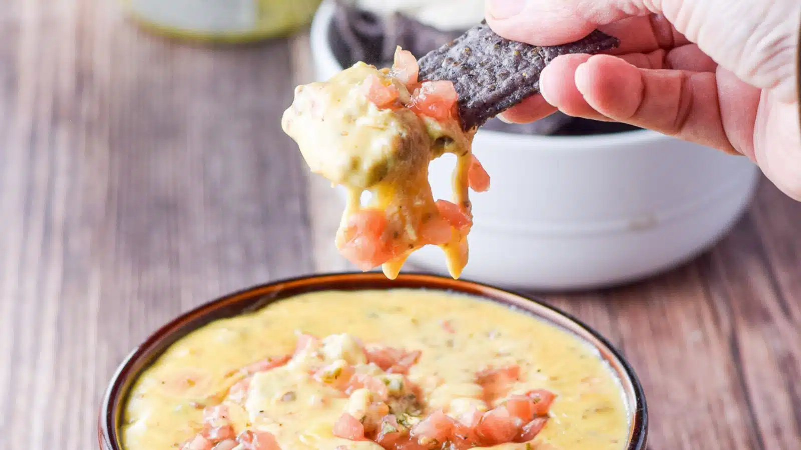 A hand holding a blue chip dipped into the cheese and tomato dip