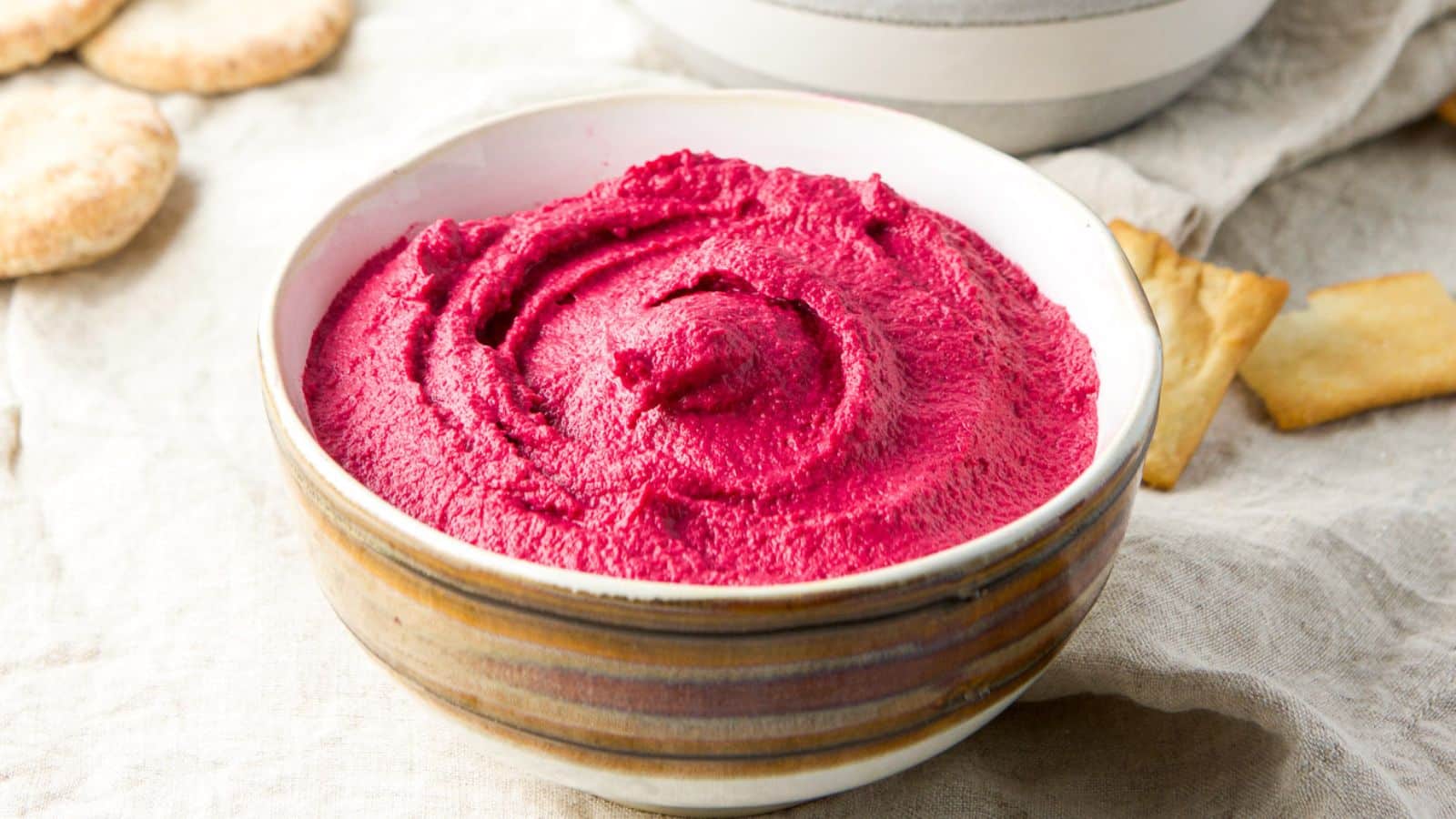 a brown bowl with red hummus with chips on the napkin and little pitas