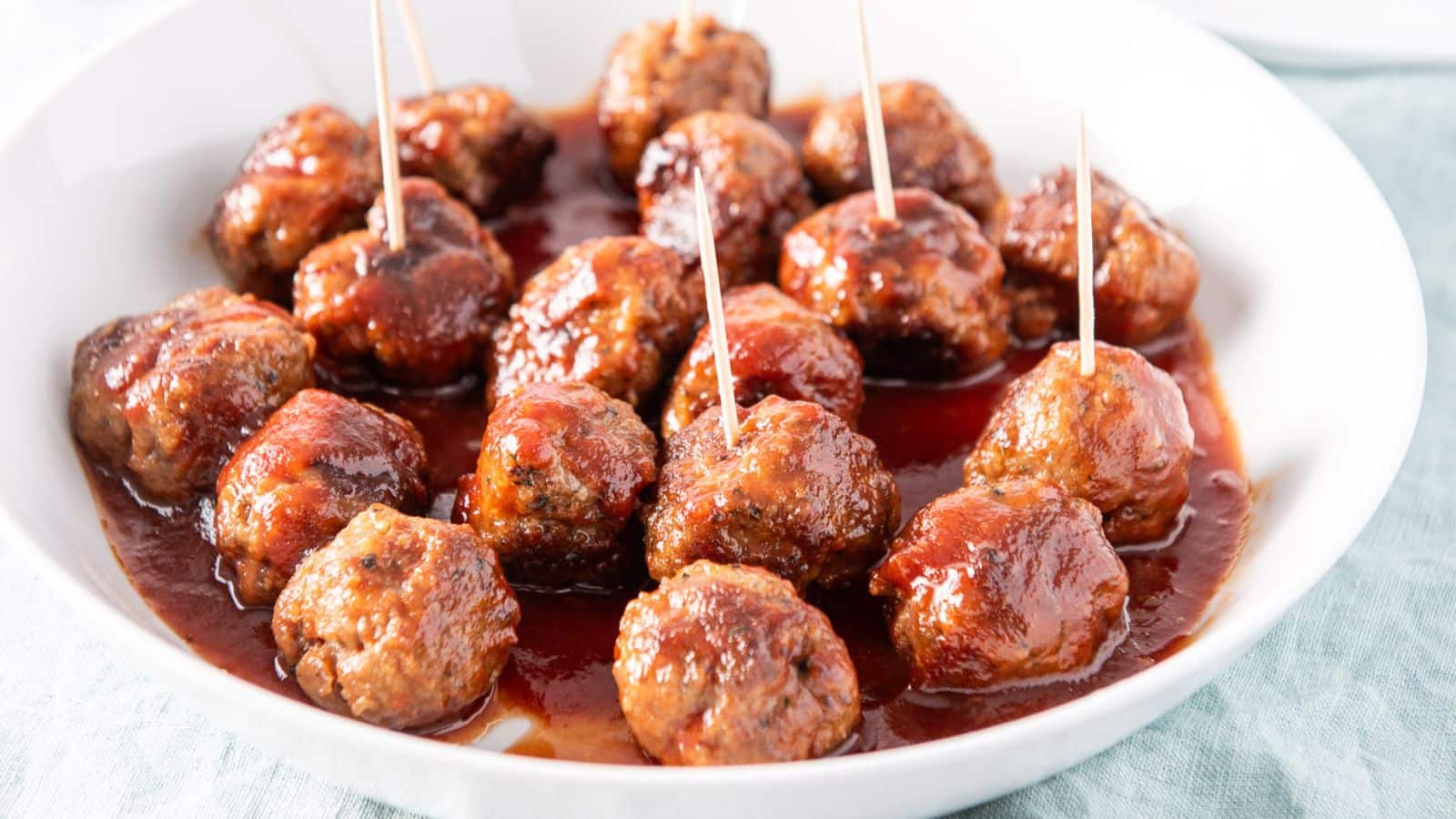 A white dish filled with meatballs with a sauce on them with toothpicks in them