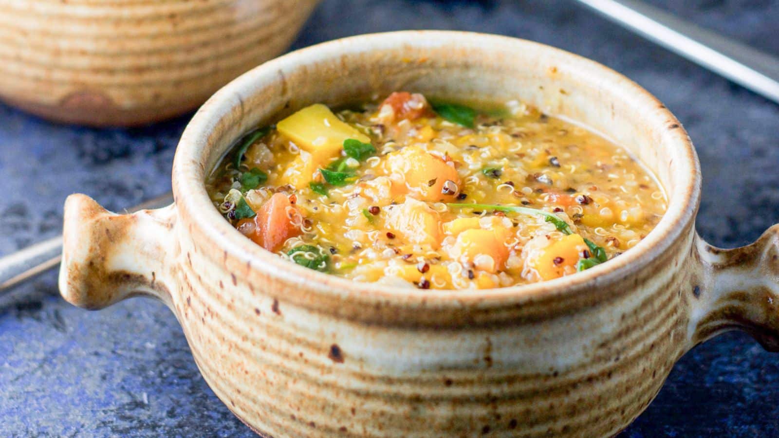 A crock with two handles filled with a stew with squash, quinoa, and more vegetables