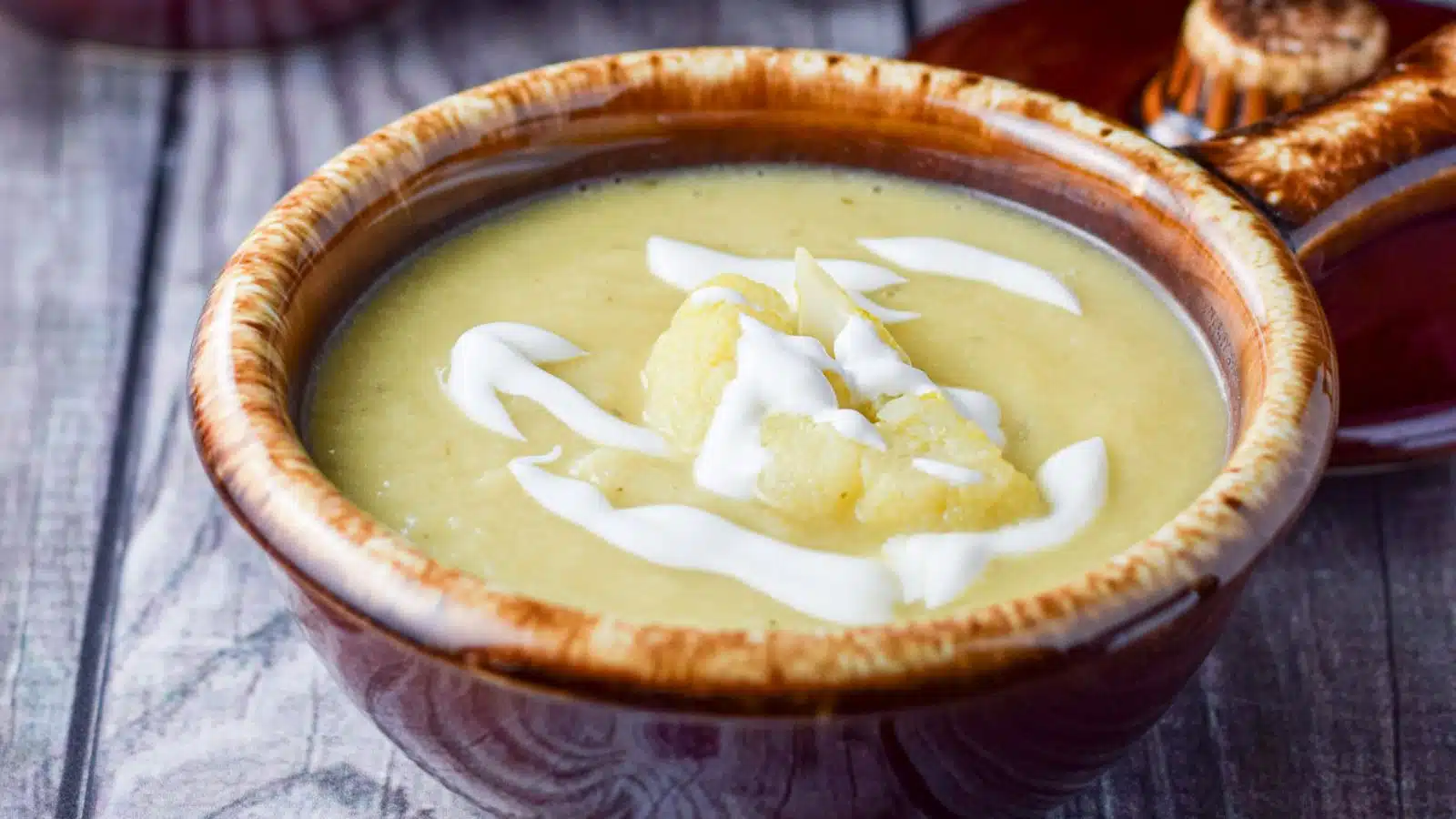 A brown bowl with cauliflower soup in it with sour cream dribbles on top