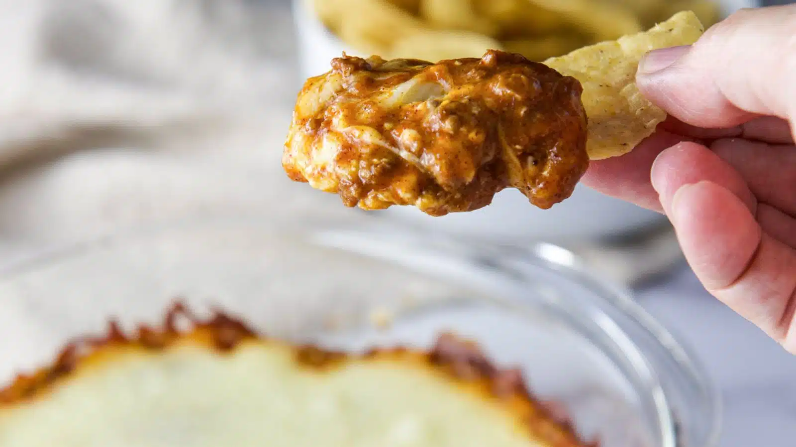 A hand holding a chip dipped in the chili dip