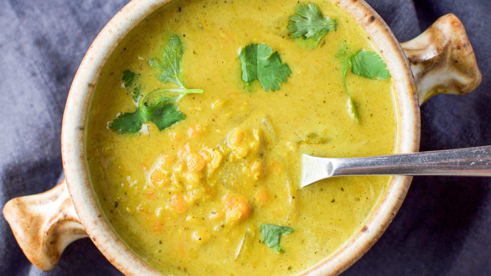 overhead view of a spoon in a bowl of curry soup with cilantro on top