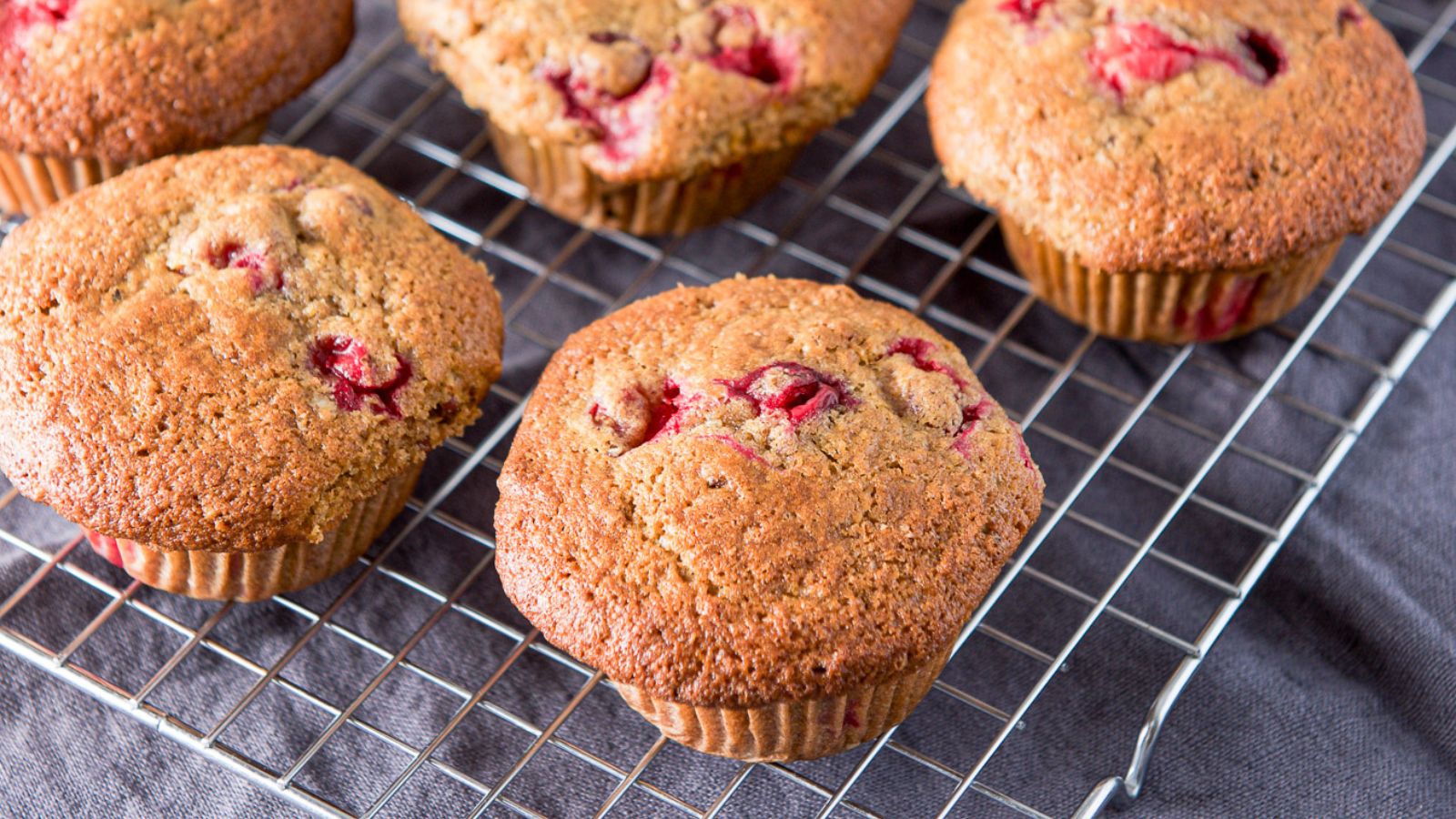 A wire rack with muffins on it with cranberries in them