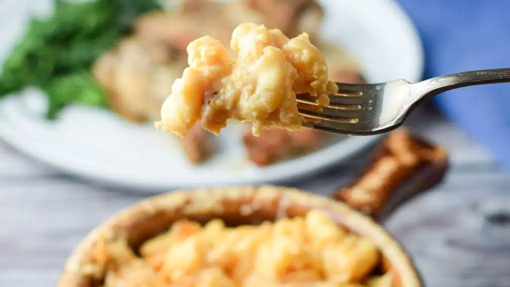 A fork filled with the macaroni held over a bowl with mac and cheese.