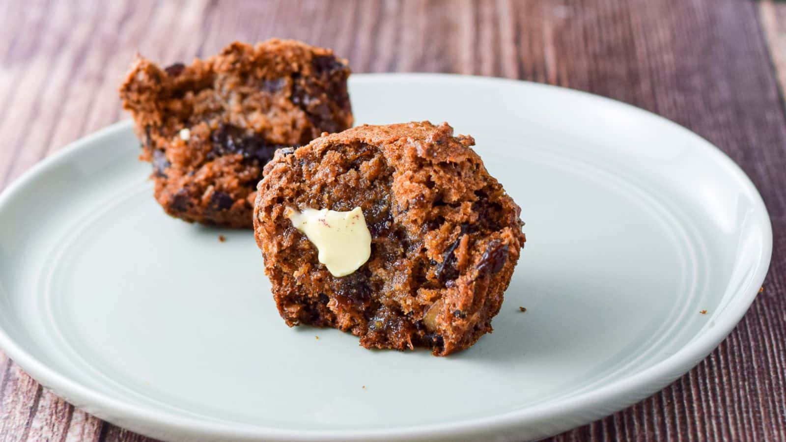 A light green plate with two halves of a muffin on it with a slab of butter on one side