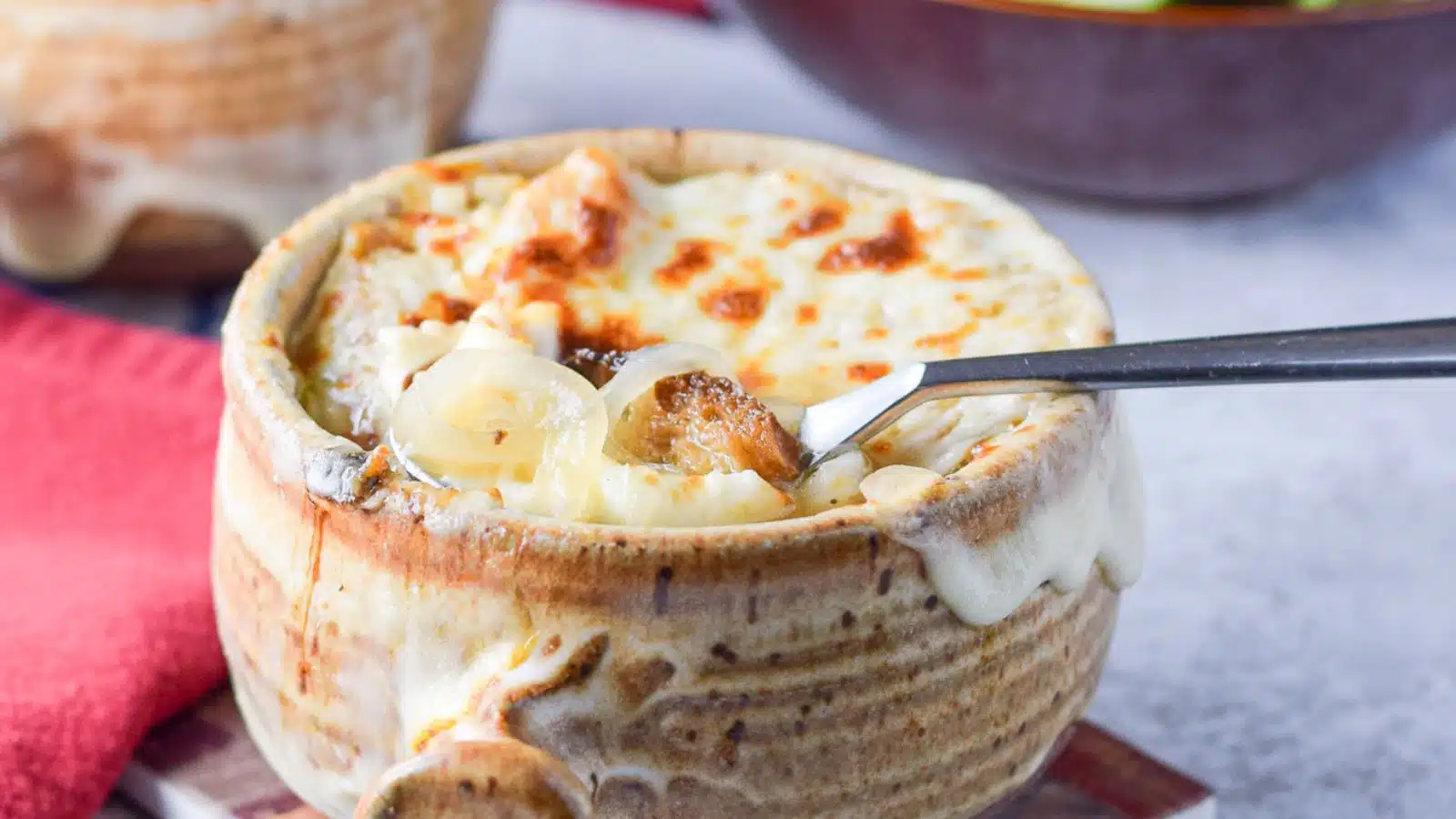 A bowl with melted cheese on top but with a spoon raising up toast and onions