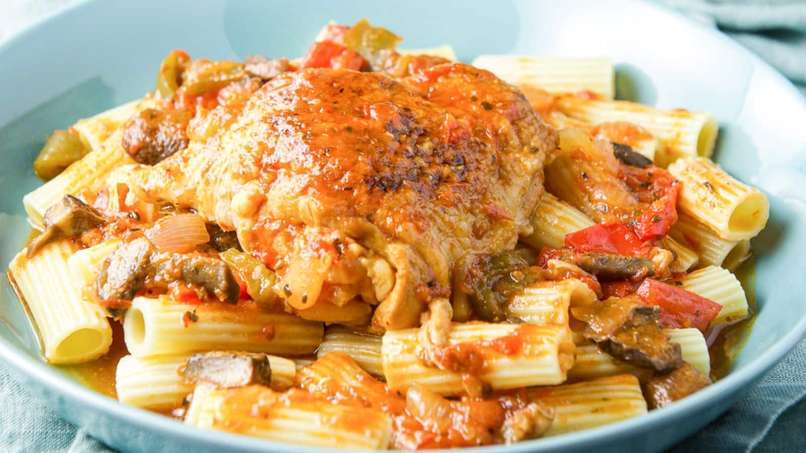 A blue green deep dish filled with pasta with chicken and red gravy over it