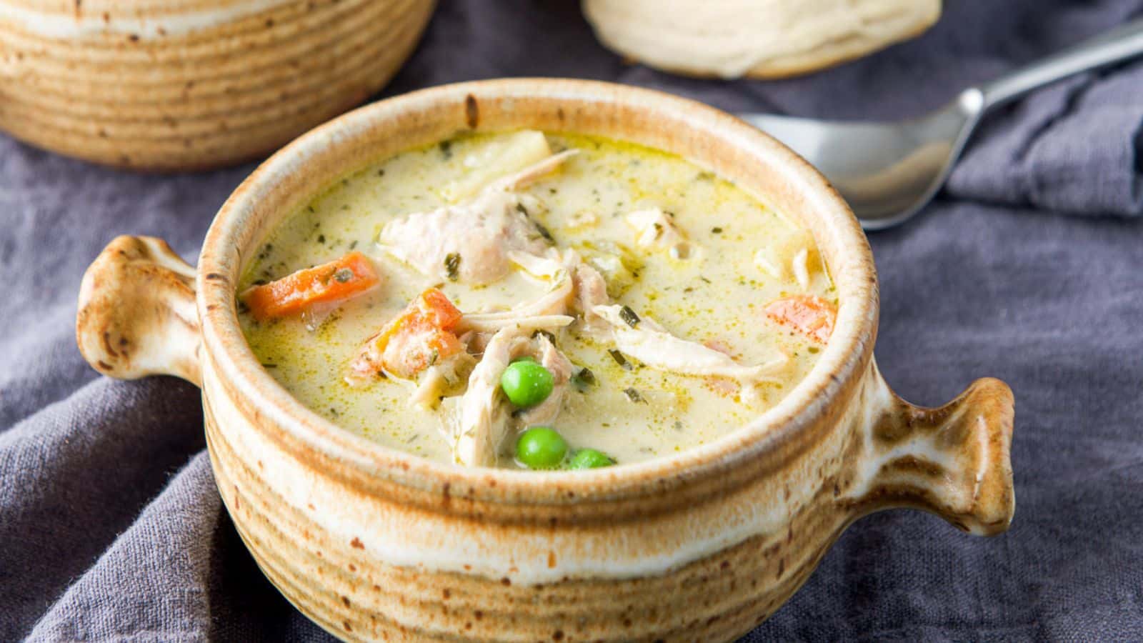 A chicken soup with peas and carrots in a crock with two handles