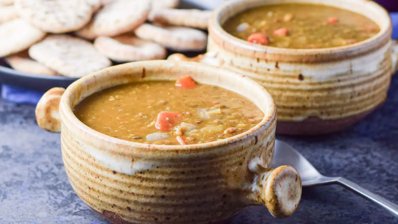 two brown crocks with lentil soup in it with little pitas in the background