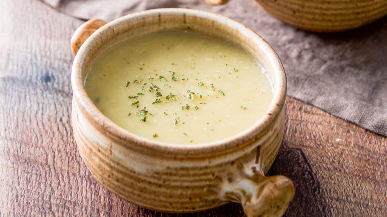 a crock with two handles filled with the potato soup with crumbled herb on top