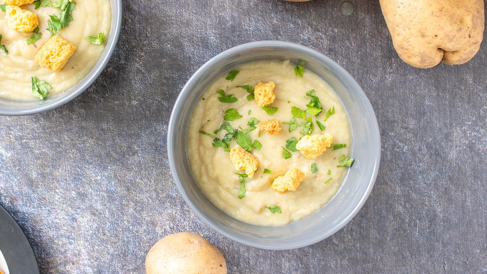 two grey bowls filled with the thick potato soup with more of the vegetable on the table