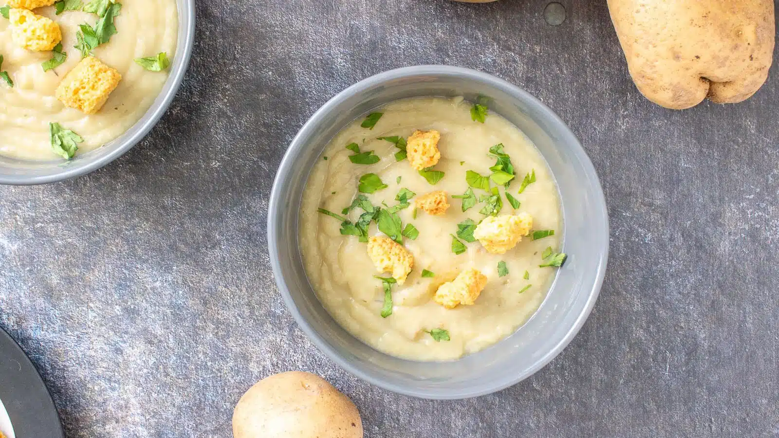 two grey bowls filled with the thick potato soup with more of the vegetable on the table