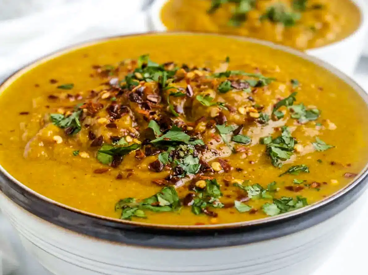 two bowls with the pumpkin soup with lots of things sprinkled on top including nuts and cilantro