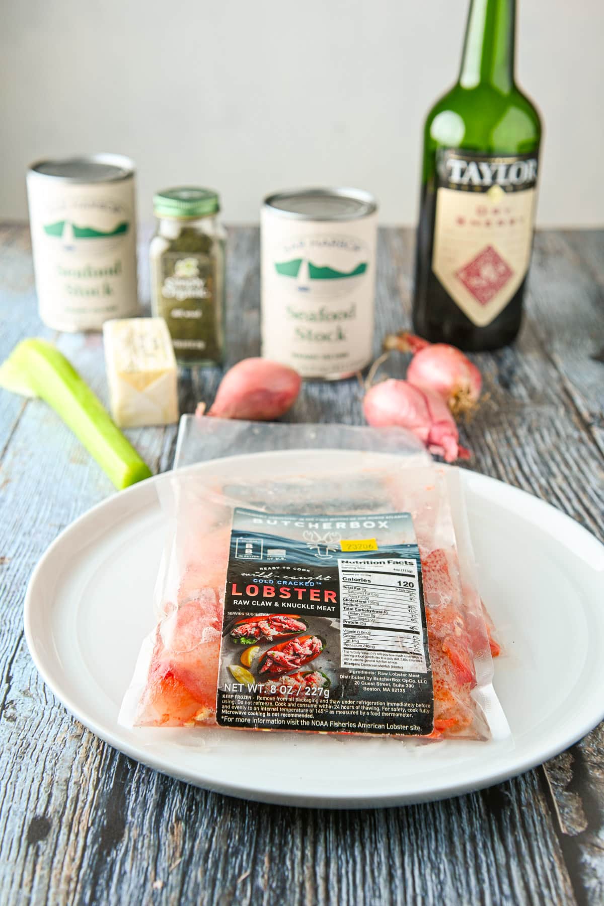 Lobster mean in plastic on a plate with celery, shallots, seafood stock, herbs, and sherry on a table