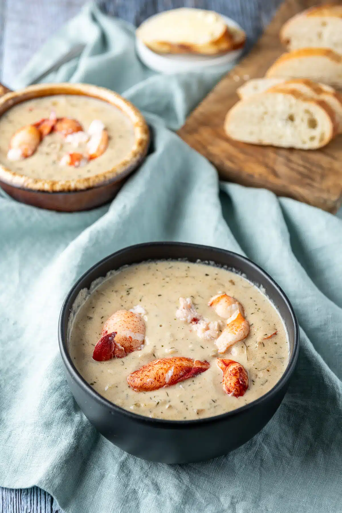 A big black bowl and a smaller crock filled with the bisque with lots of lobster pieces on top along with bread in the back