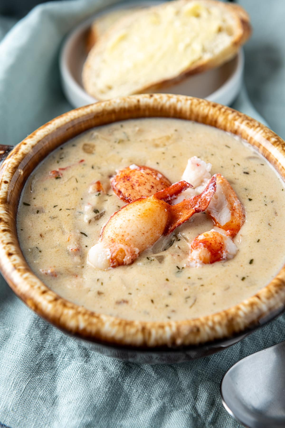 Close up view of lobster on a bisque in a crock and bread in the background