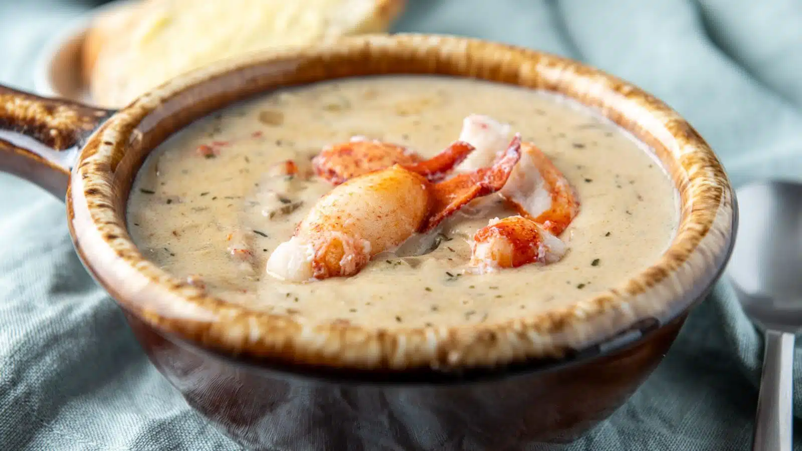 A horizontal photo of a brown crock with the bisque in it with big pieces of lobster pieces on top