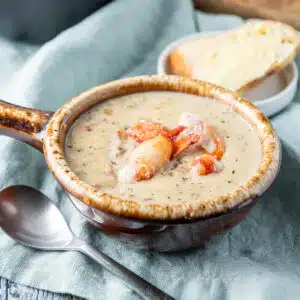 a crock with a handle filled with the bisque with lobster on top and bread in the back